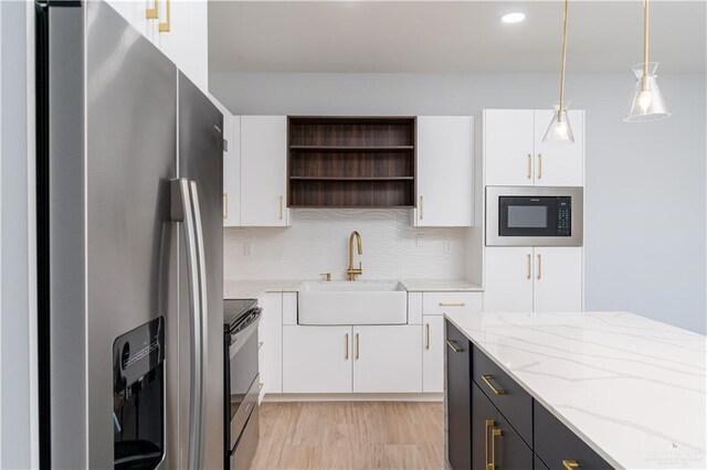 kitchen featuring light stone countertops, stainless steel appliances, sink, white cabinetry, and hanging light fixtures