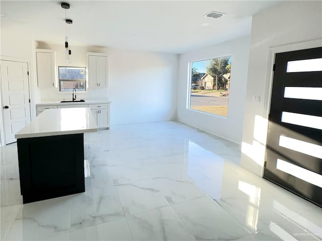 kitchen with white cabinetry, a kitchen island, sink, and decorative light fixtures