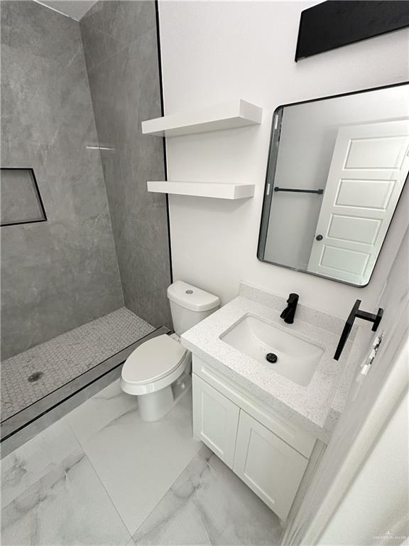 bathroom with vanity, a tile shower, and toilet