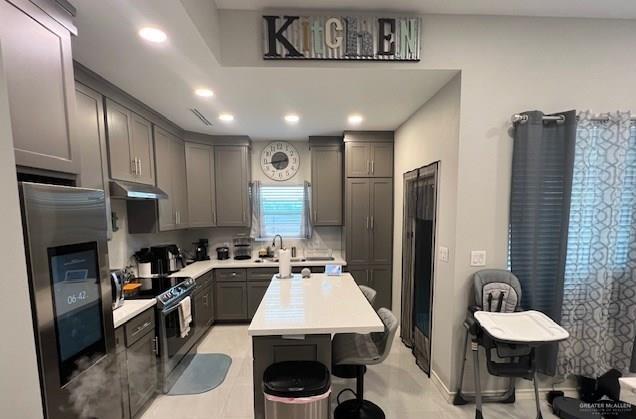 kitchen featuring appliances with stainless steel finishes, sink, gray cabinets, a kitchen island, and a breakfast bar area