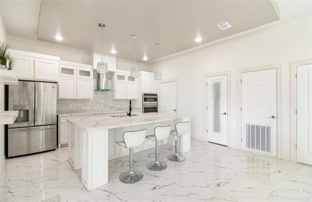 kitchen with marble finish floor, a kitchen island with sink, a sink, appliances with stainless steel finishes, and wall chimney exhaust hood