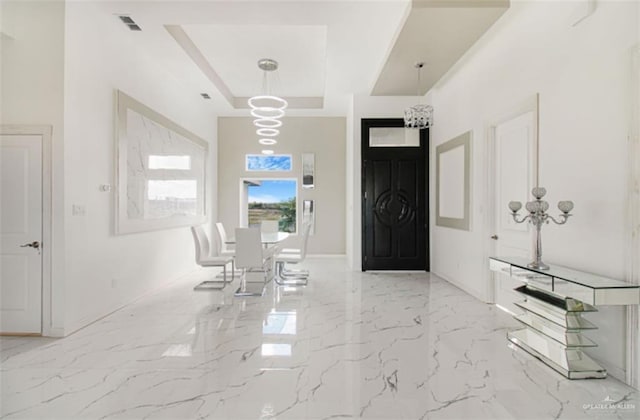 foyer entrance featuring visible vents, a raised ceiling, marble finish floor, an inviting chandelier, and baseboards