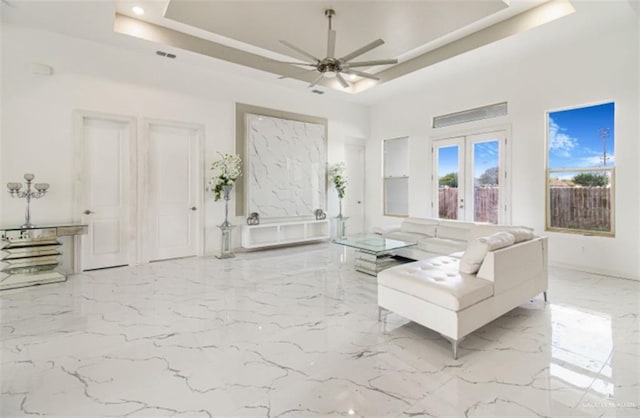 living room featuring a ceiling fan, a tray ceiling, french doors, and marble finish floor