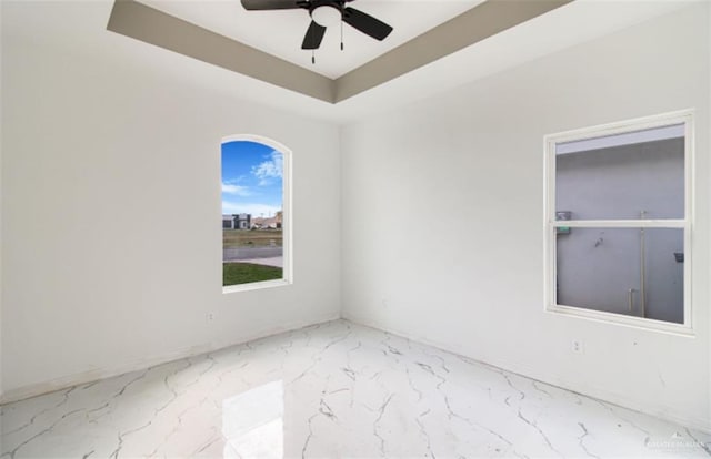 empty room with a raised ceiling, marble finish floor, and ceiling fan