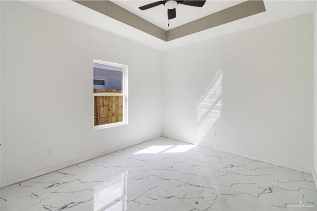 empty room featuring marble finish floor, a raised ceiling, and a ceiling fan