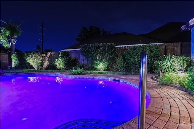 pool at twilight with a patio area and a fenced backyard