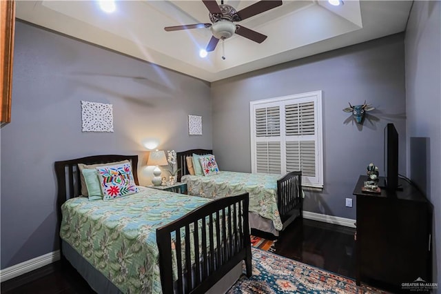 bedroom with a tray ceiling, wood finished floors, a ceiling fan, and baseboards