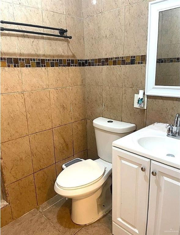 bathroom featuring toilet, tile patterned flooring, tile walls, and vanity