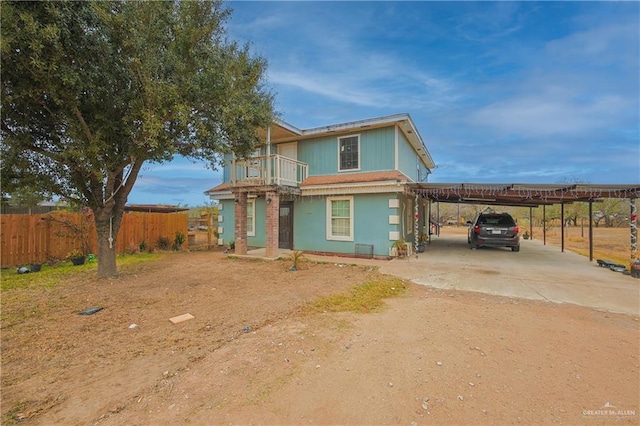 view of front of house featuring driveway, an attached carport, fence, and a balcony