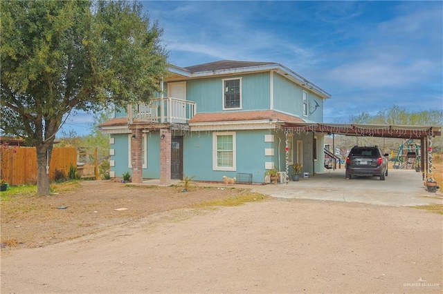 view of front of house with a balcony, dirt driveway, fence, and an attached carport