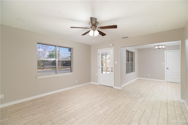 spare room featuring ceiling fan with notable chandelier, light hardwood / wood-style flooring, and a healthy amount of sunlight