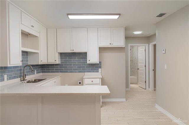 kitchen with sink, white cabinetry, tasteful backsplash, light hardwood / wood-style floors, and kitchen peninsula