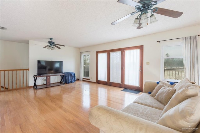 living room with ceiling fan, a textured ceiling, and light hardwood / wood-style floors