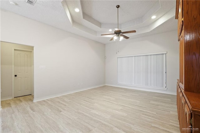 interior space with light wood-style floors, baseboards, ceiling fan, a textured ceiling, and a raised ceiling
