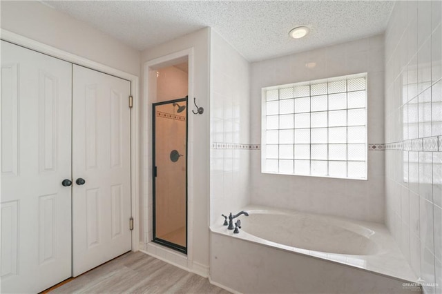 bathroom with a textured ceiling, wood finished floors, a garden tub, and a stall shower
