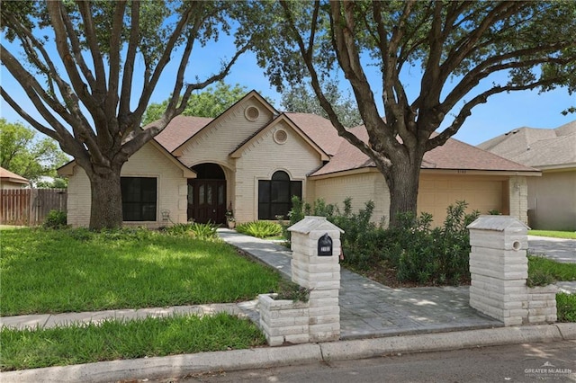 view of front facade featuring a front lawn, fence, brick siding, a shingled roof, and an attached garage