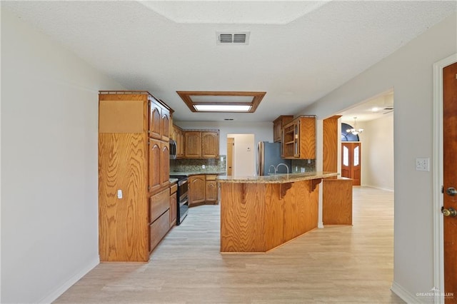 kitchen featuring a kitchen bar, visible vents, appliances with stainless steel finishes, light wood-type flooring, and a peninsula