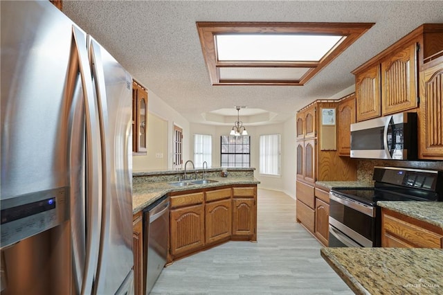 kitchen featuring appliances with stainless steel finishes, a sink, a textured ceiling, brown cabinetry, and a peninsula