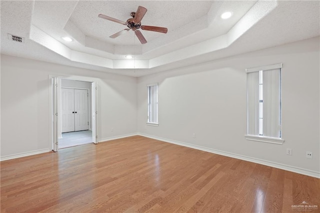 unfurnished room with light wood-type flooring, a ceiling fan, a raised ceiling, and baseboards