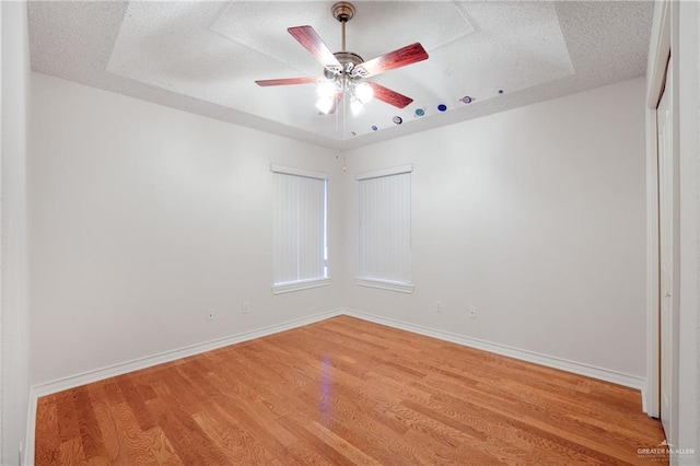 empty room featuring baseboards, a ceiling fan, light wood finished floors, and a textured ceiling