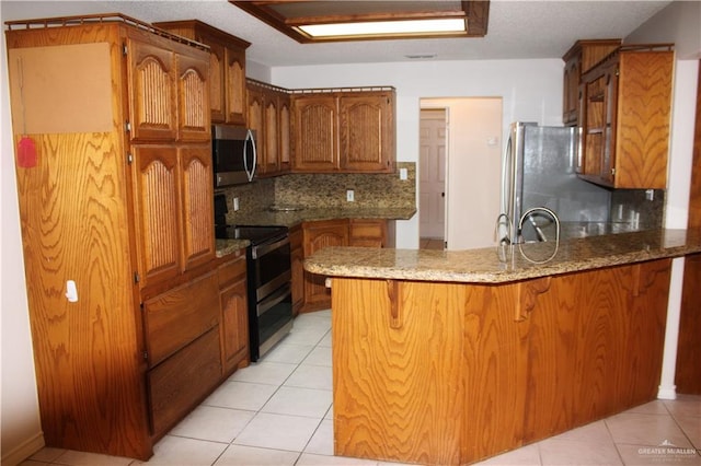 kitchen with backsplash, sink, light tile patterned floors, kitchen peninsula, and stainless steel appliances