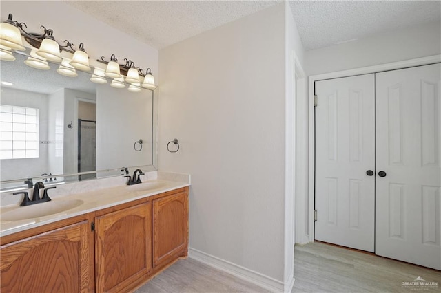 full bath featuring double vanity, a textured ceiling, a sink, and wood finished floors