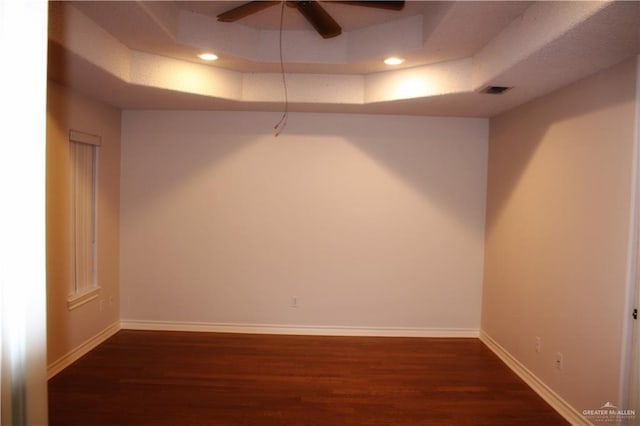 unfurnished room featuring a raised ceiling, ceiling fan, and dark hardwood / wood-style flooring