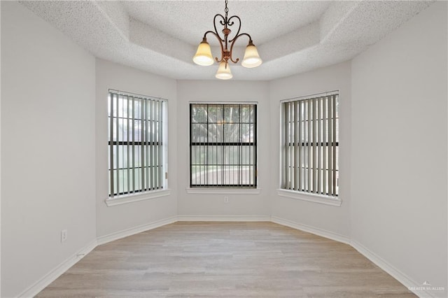 unfurnished room featuring a textured ceiling, a tray ceiling, a chandelier, and light wood finished floors
