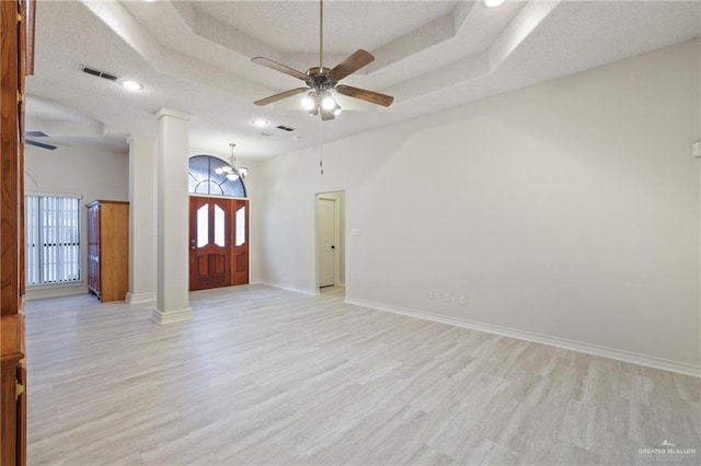 unfurnished living room featuring ornate columns, plenty of natural light, ceiling fan with notable chandelier, and light wood-type flooring