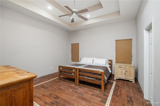 bedroom with a raised ceiling, ceiling fan, and dark wood-type flooring