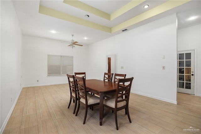 dining room with ceiling fan, a raised ceiling, and light hardwood / wood-style flooring