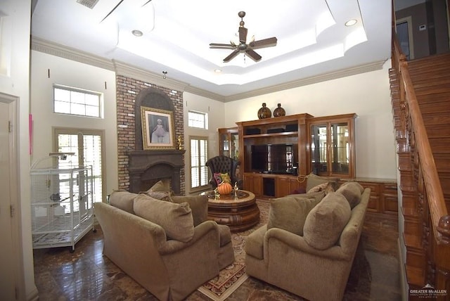 living room with ornamental molding, a tray ceiling, ceiling fan, a fireplace, and a high ceiling