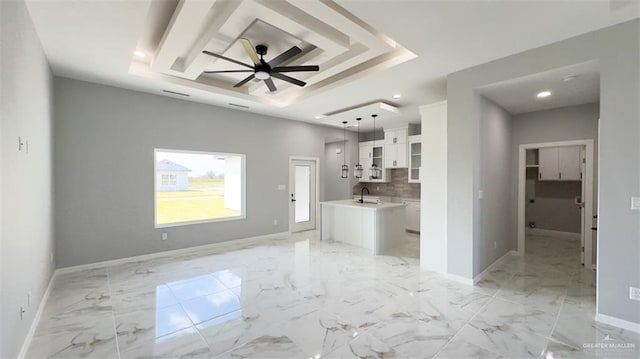 unfurnished living room with ceiling fan, sink, and a tray ceiling