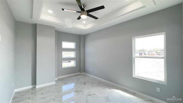 empty room featuring a tray ceiling, ceiling fan, and a healthy amount of sunlight