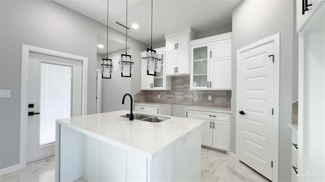 kitchen featuring pendant lighting, white cabinets, sink, decorative backsplash, and an island with sink