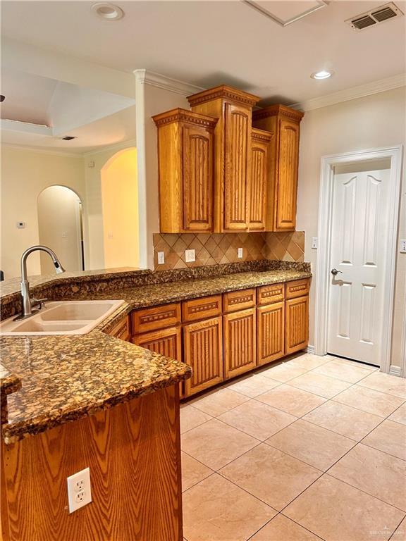 2401 S Gardenia St, Pharr, TX 78577 - kitchen featuring a sink, arched walkways, crown molding, decorative backsplash, and brown cabinets