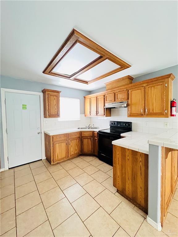 kitchen with tile countertops, backsplash, sink, light tile patterned floors, and black range with electric cooktop