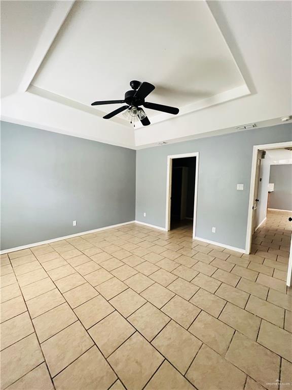 tiled empty room featuring a tray ceiling and ceiling fan