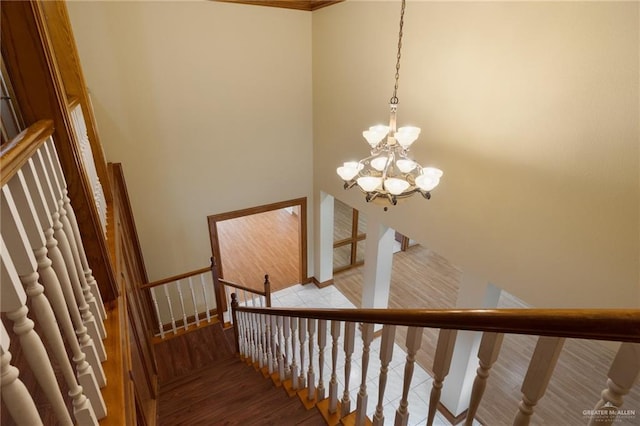 stairs with wood-type flooring, a towering ceiling, and a notable chandelier