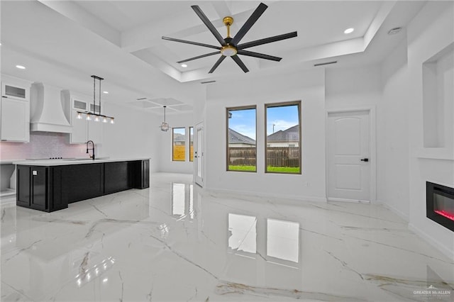 kitchen featuring white cabinets, a large island, hanging light fixtures, light countertops, and premium range hood