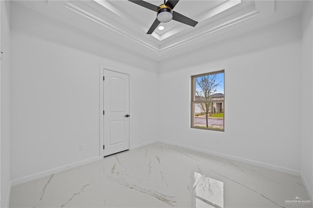 spare room featuring marble finish floor, baseboards, a tray ceiling, and a ceiling fan