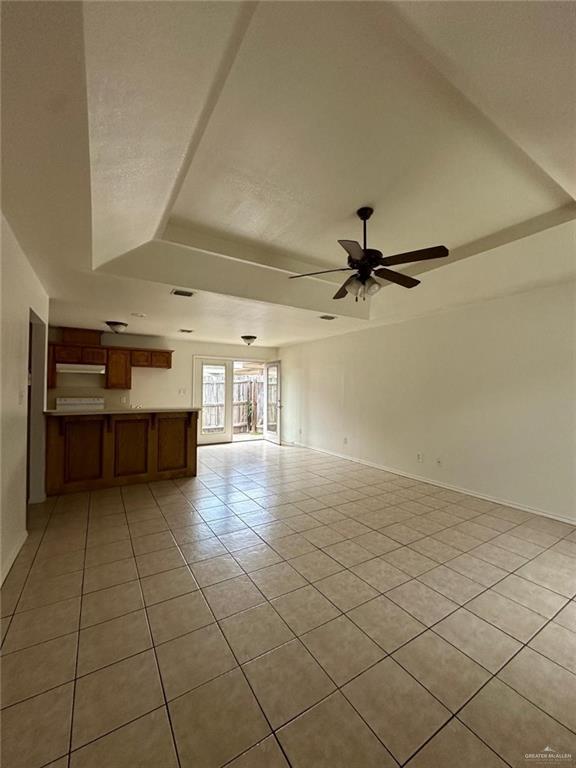 unfurnished living room with a tray ceiling, ceiling fan, light tile patterned flooring, and baseboards