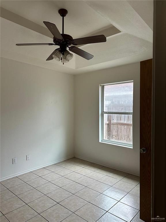 spare room featuring a raised ceiling, light tile patterned floors, baseboards, and a ceiling fan