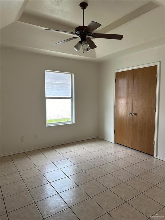 unfurnished bedroom with a closet, light tile patterned floors, a tray ceiling, and baseboards