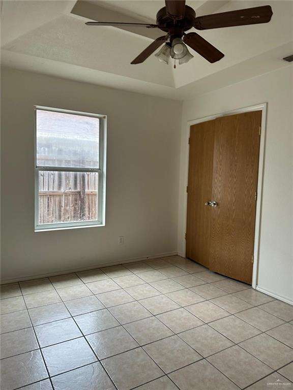 empty room with light tile patterned floors, baseboards, a raised ceiling, visible vents, and a ceiling fan