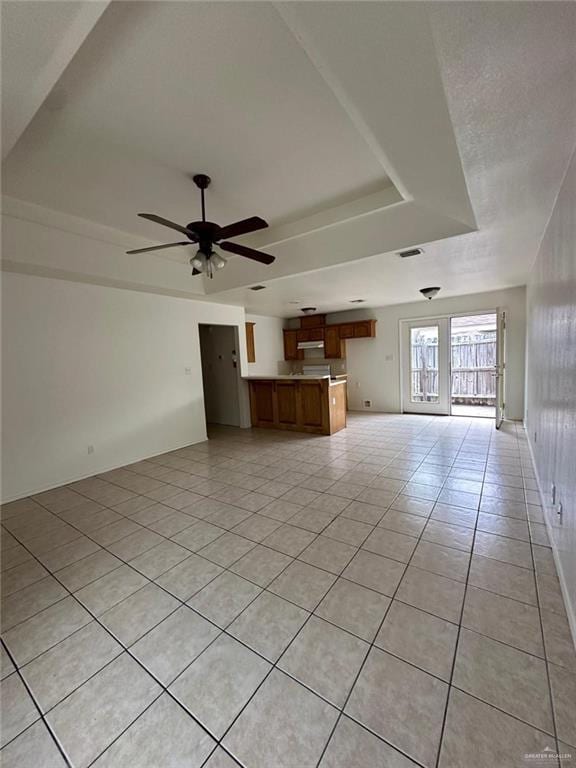unfurnished living room featuring a tray ceiling, light tile patterned flooring, ceiling fan, and visible vents