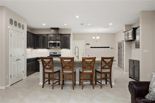 kitchen with appliances with stainless steel finishes, an island with sink, light stone countertops, and backsplash