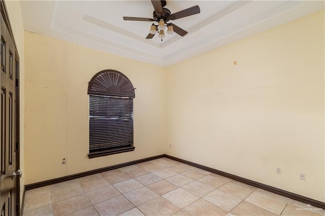 empty room with a raised ceiling, ceiling fan, and light tile patterned floors