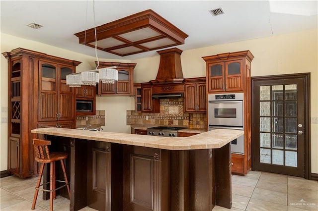 kitchen with decorative backsplash, light tile patterned floors, tile counters, a kitchen island, and stainless steel appliances