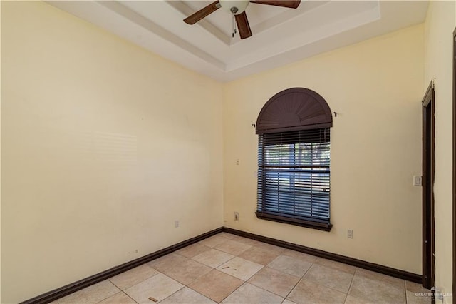 tiled empty room with a raised ceiling and ceiling fan